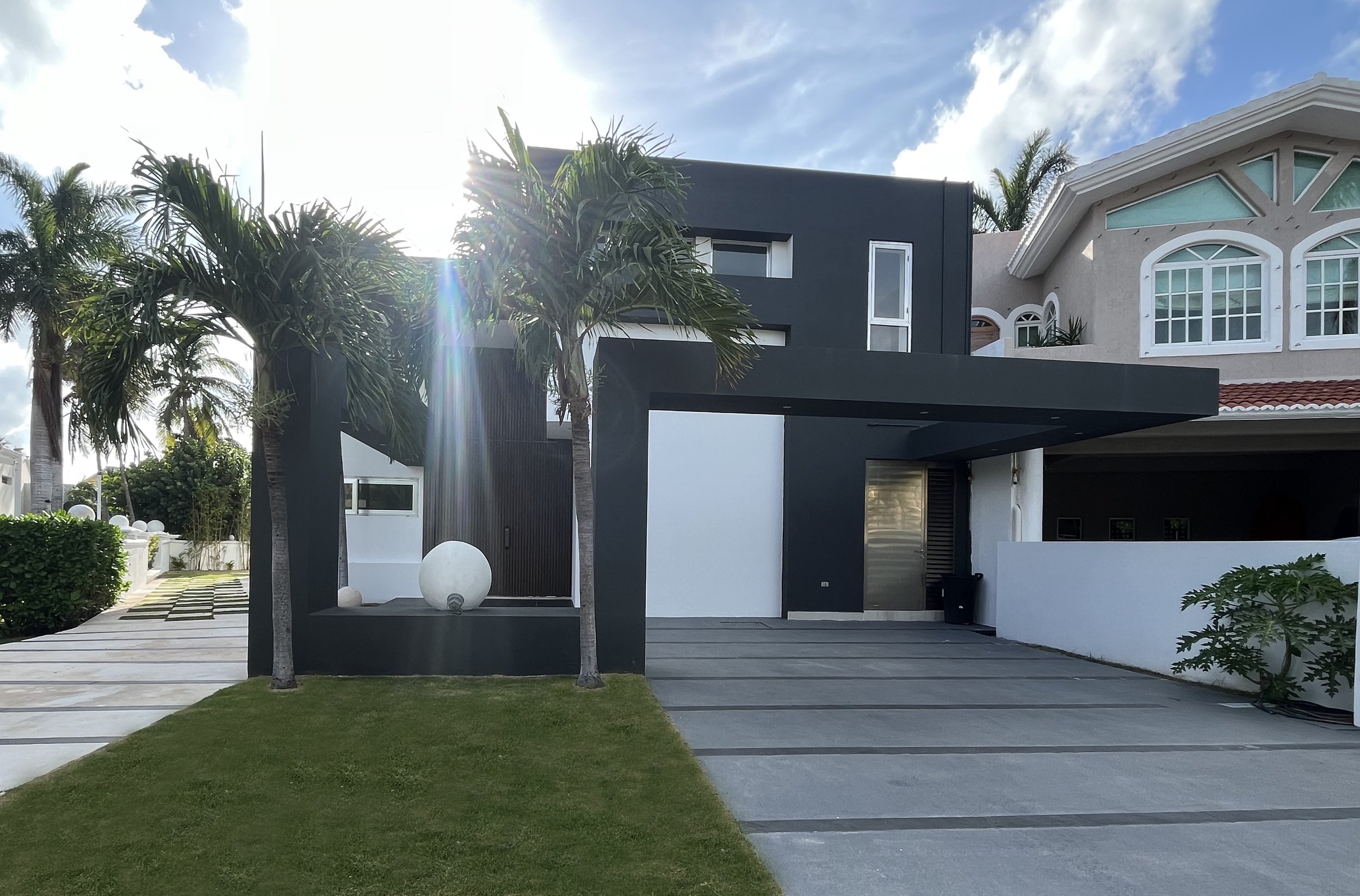 Modern house with palm trees and driveway, featuring geometric architecture and a white and dark gray color scheme.