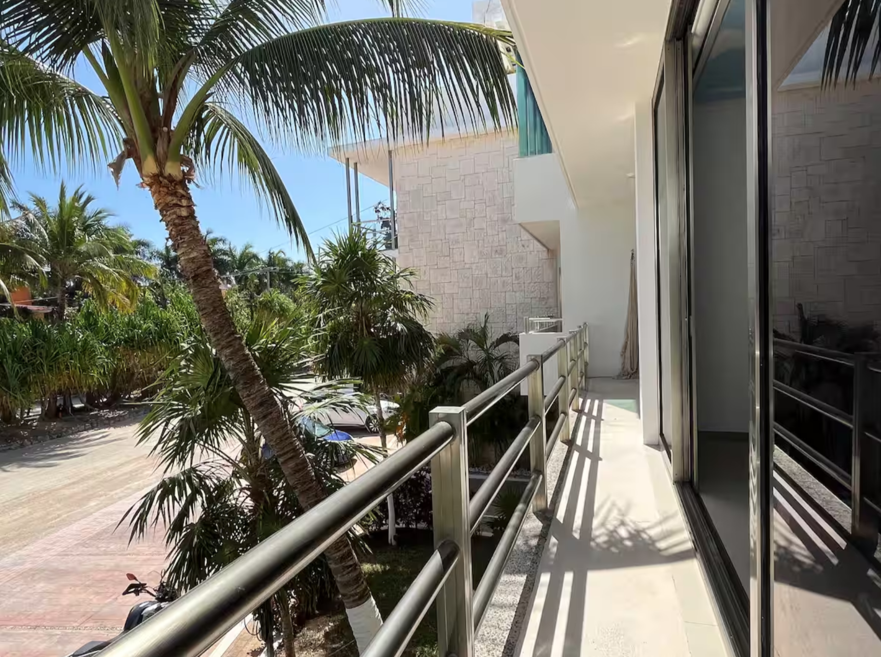 Balcony view with palm trees, glass doors, and a modern building exterior.