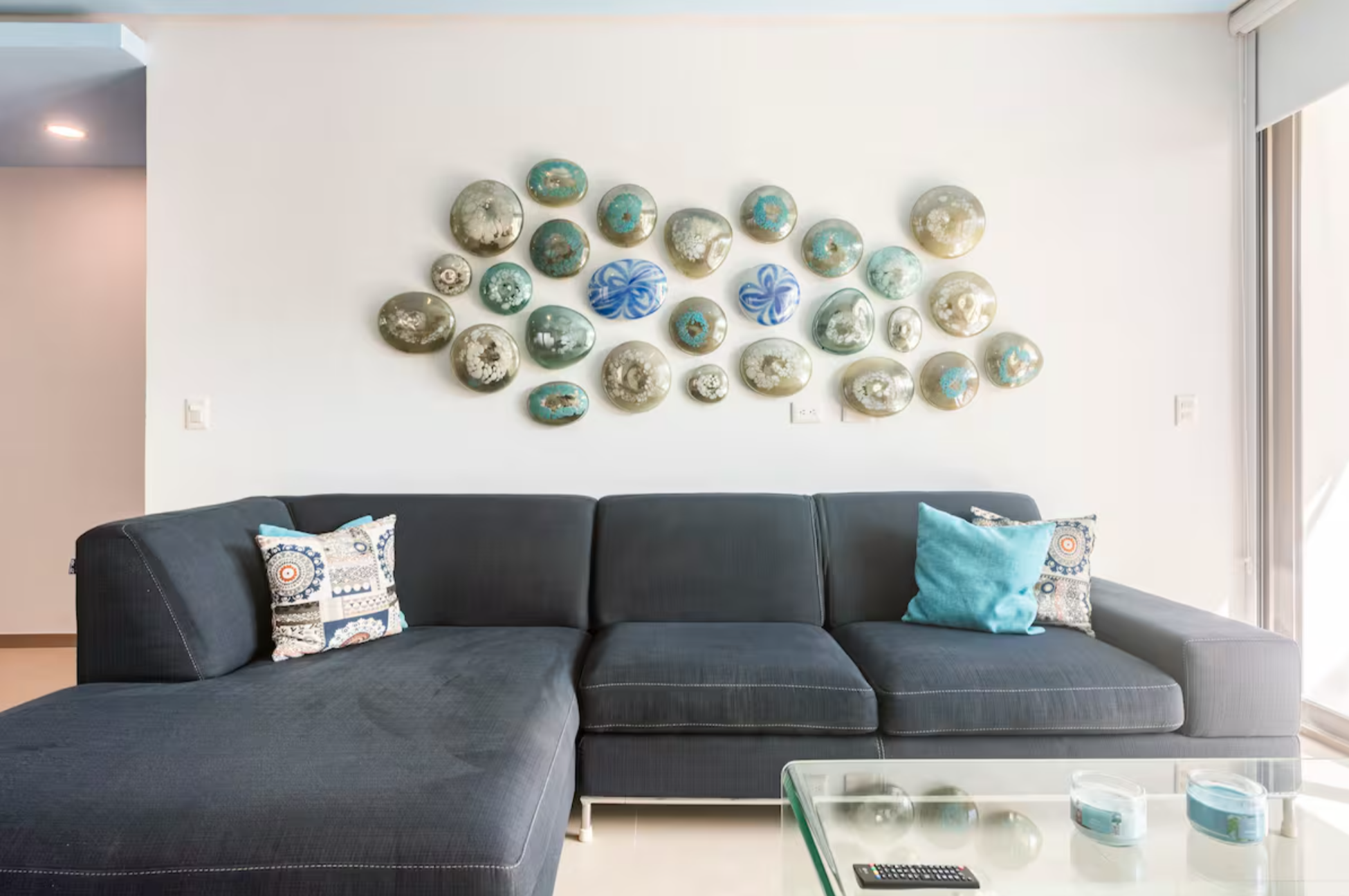 Modern living room with dark gray sectional sofa, decorative pillows, glass coffee table, and abstract wall art with circular shapes.