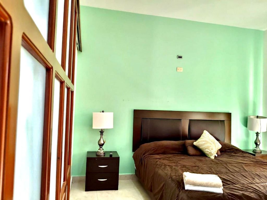 Bedroom with brown bed, green walls, two lamps, nightstands, and folded towels on the bed.