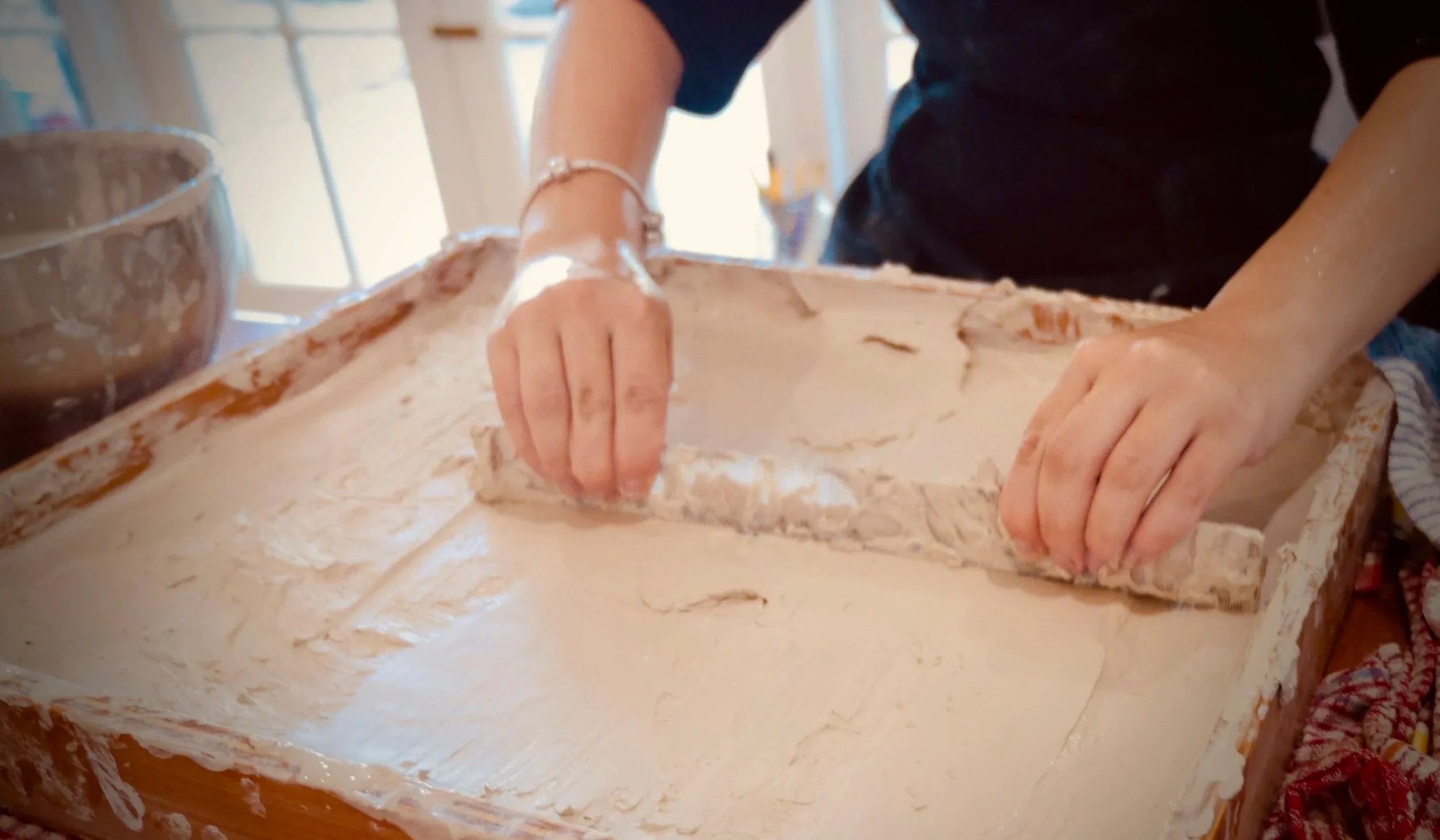 Person kneading dough on a wooden surface in a bright kitchen.