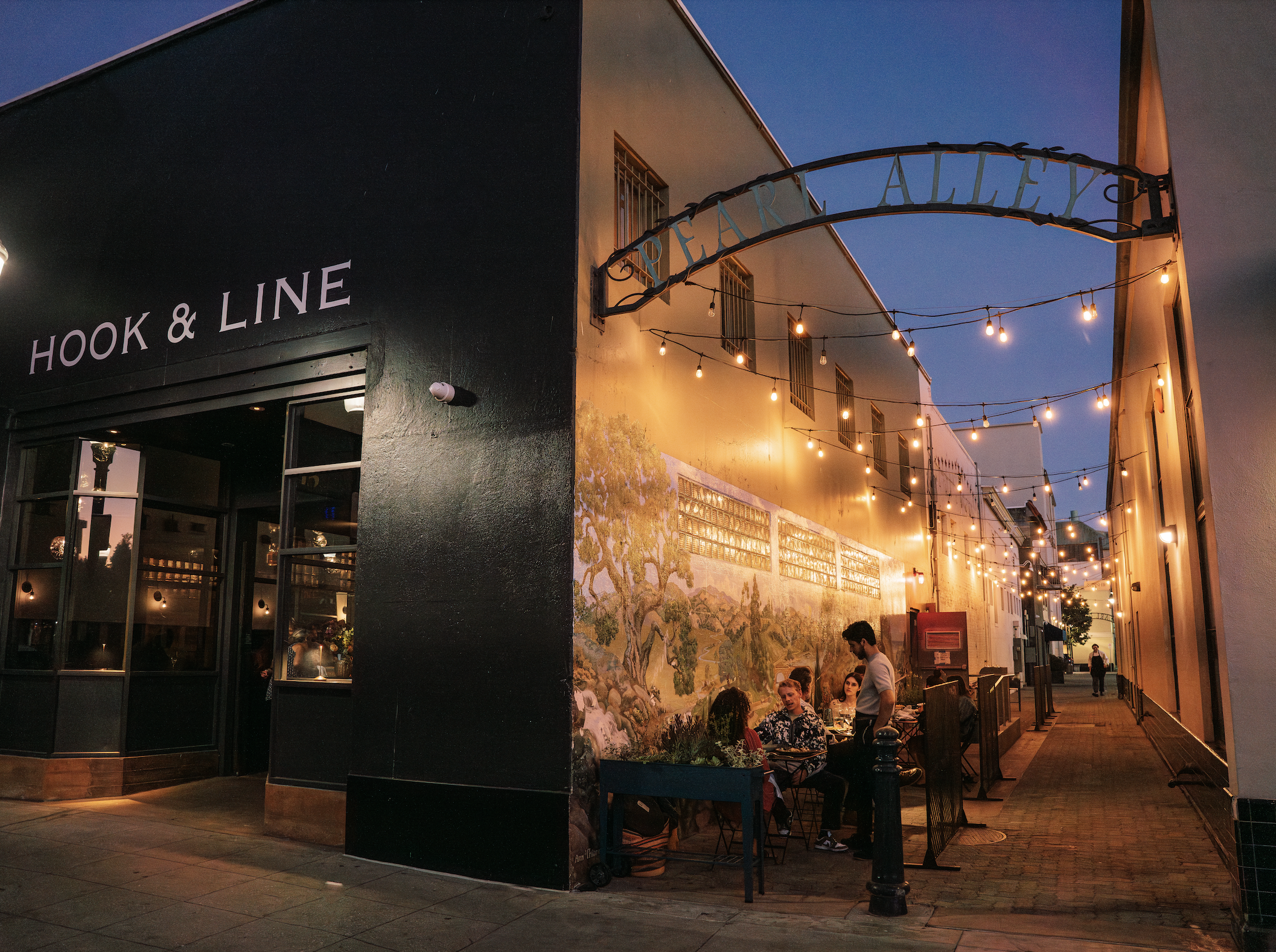 An image of pearl alley lined with outdoor, tables and chairs with people dining.