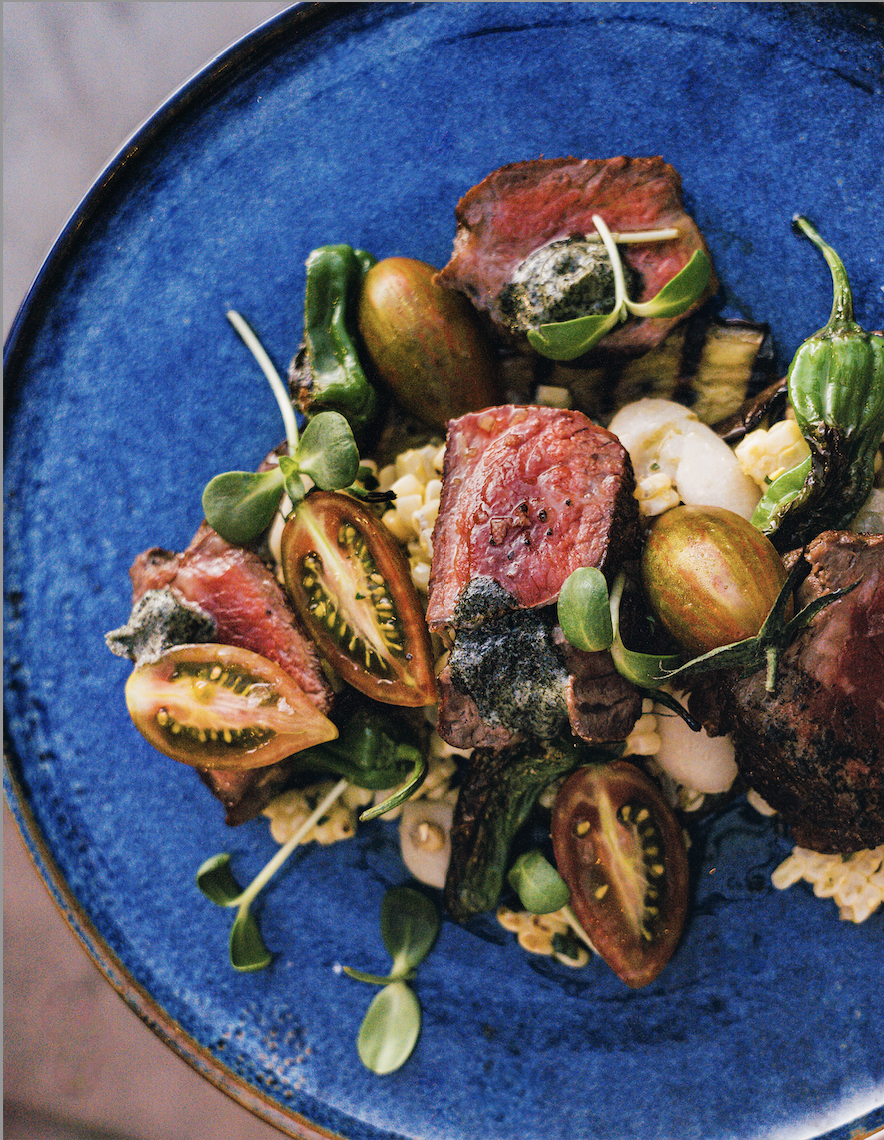 A blue plate with pieces of steak, tomatoes and sprouts