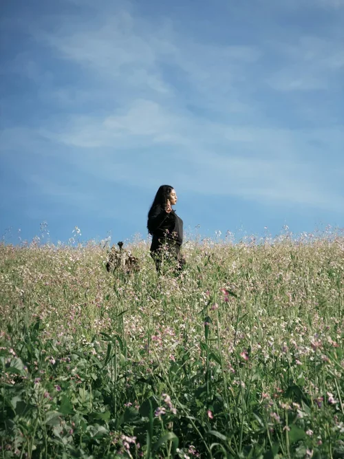 Woman standing peacefully in a wildflower field under a blue sky, representing calmness, emotional healing, and anxiety therapy support.