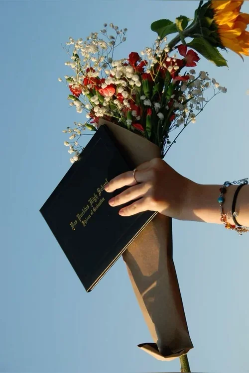 Hand holding a bouquet of flowers and a journal against a bright sky, symbolizing healing, emotional processing, and EMDR therapy support.