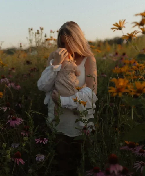Mother holding her baby in a wildflower field during golden hour, representing motherhood, bonding, emotional support, and perinatal therapy.