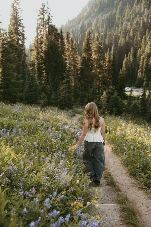 Person walking along a peaceful mountain trail surrounded by wildflowers and pine trees, symbolizing healing, growth, and trauma therapy support.