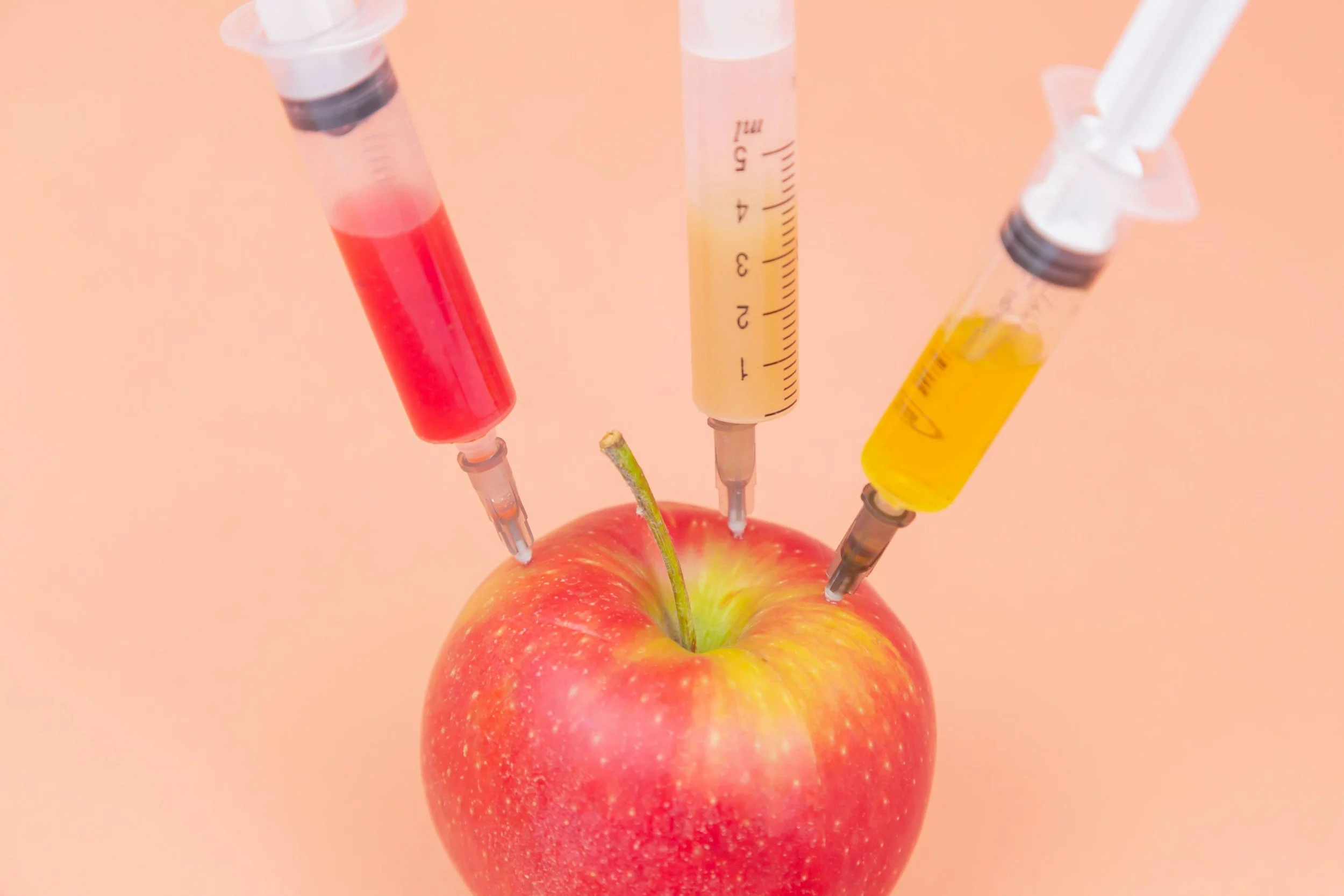 Red apple with three syringes injecting colored liquids