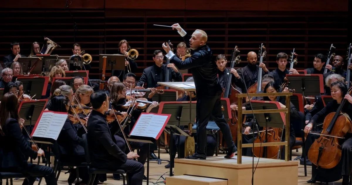 Conductor leading an orchestra with string and brass sections on stage
