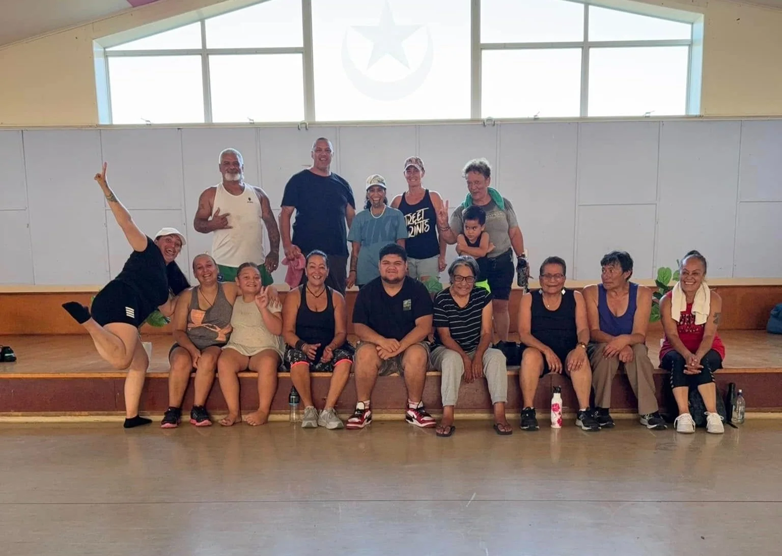 Group of people posing together on a wooden stage in a gym or indoor recreational space.