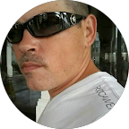 Close-up of a man wearing sunglasses, with a serious expression, outdoors.