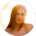 Portrait of a young woman with long hair, illuminated by warm sunlight, against a bright background.