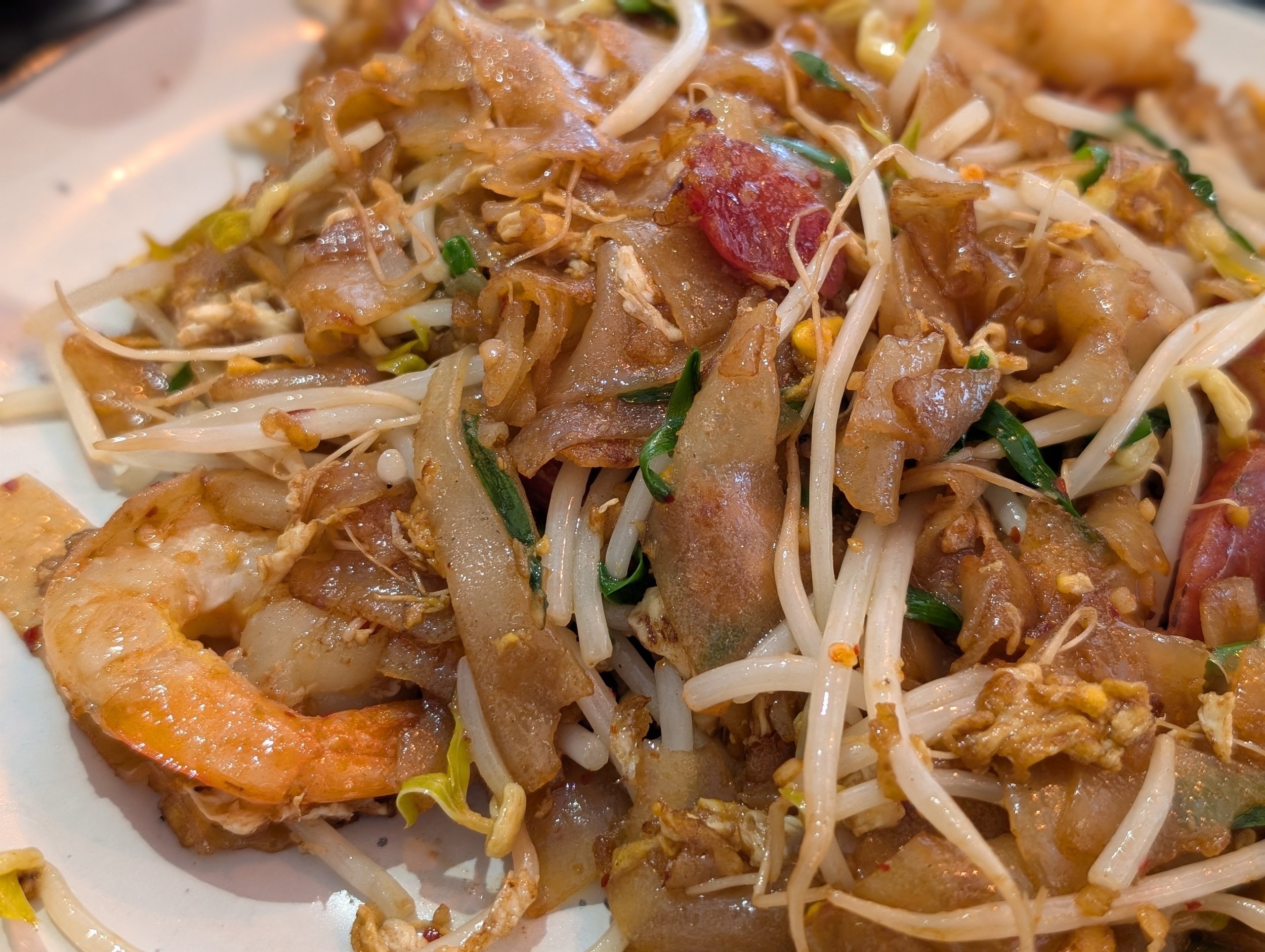 Close-up of a plate of Asian-style fried noodles with shrimp, bean sprouts, green onions, and sliced meat.