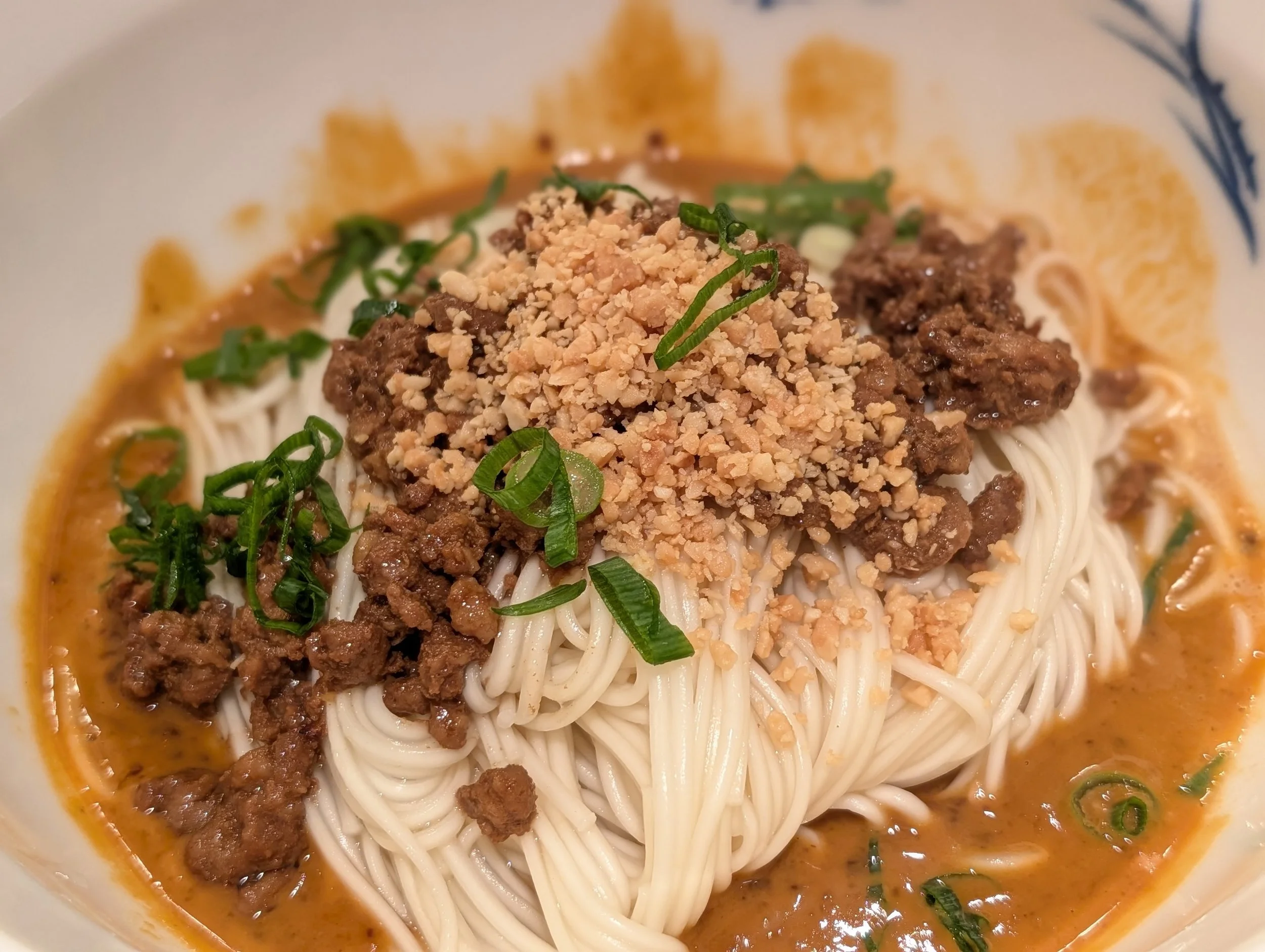 Dan Dan Noodles that combine rich sesame paste or peanut butter with a fiery, aromatic chili oil, creating a deeply complex, savoury, and spicy flavour profile; topped with finely minced or ground pork (or beef) stir-fried until crispy, often seasone