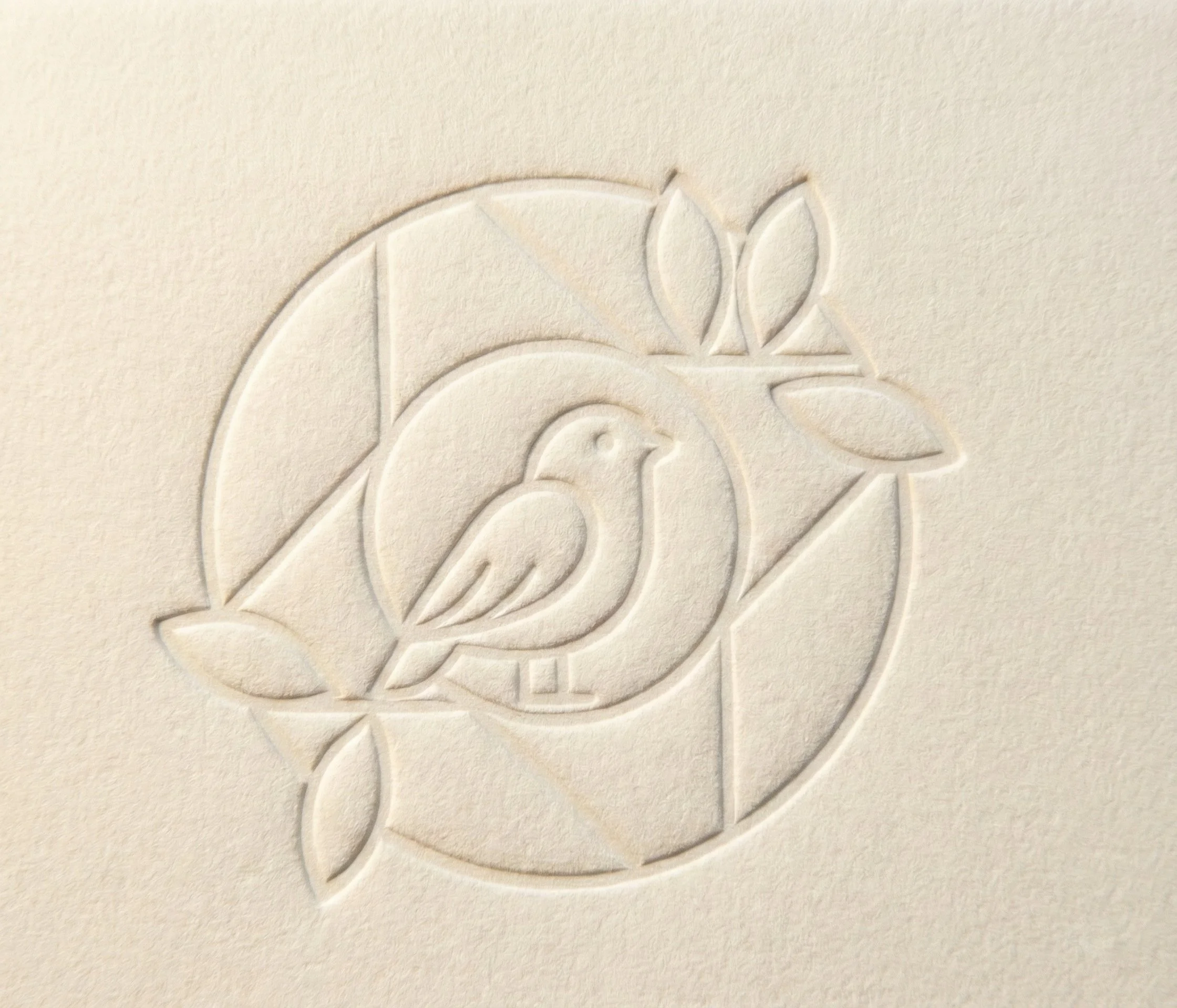 Embossed design of a bird perched on a branch with leaves, enclosed in a circle on cream-colored paper.