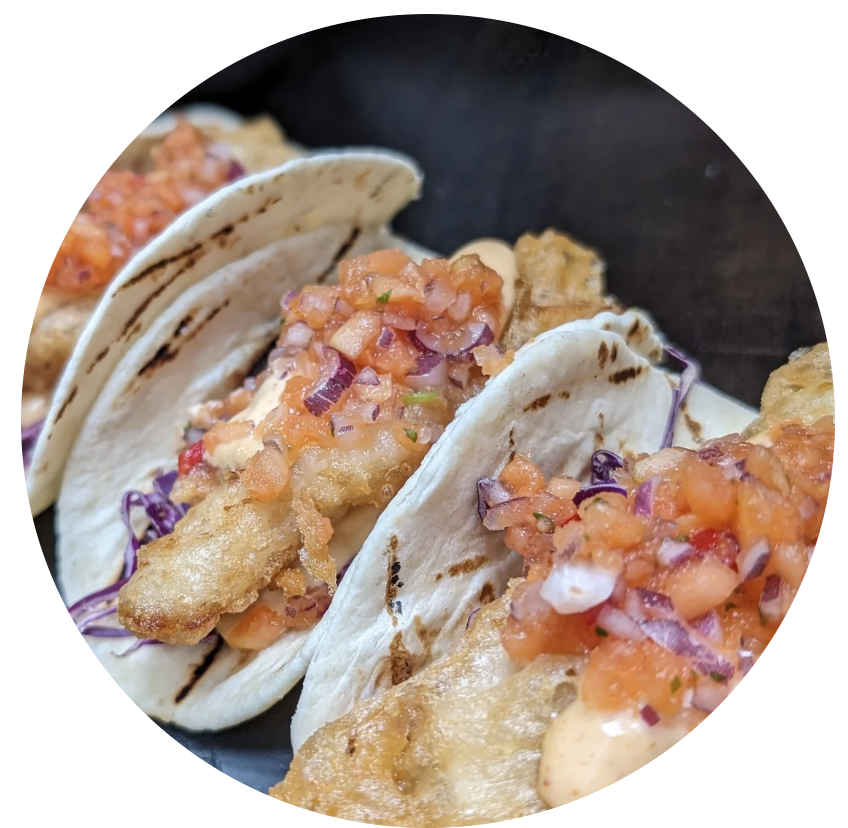 Three fish tacos with battered fish, shredded purple cabbage, and tomato-based salsa in soft flour tortillas.