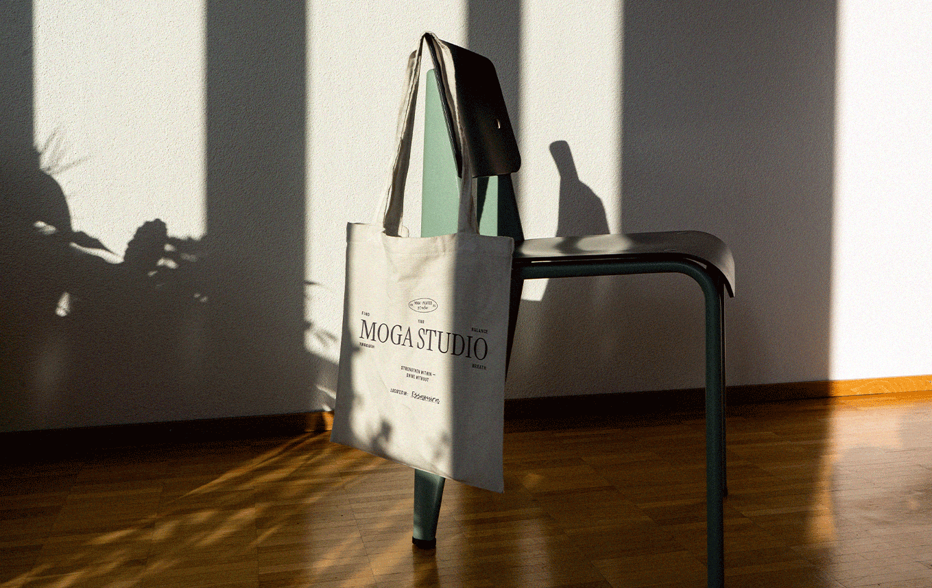 Une chaise de bureau en métal avec une sacoche en toile blanche suspendue dessus, située dans une pièce illuminée par la lumière du soleil créant des ombres sur le mur.