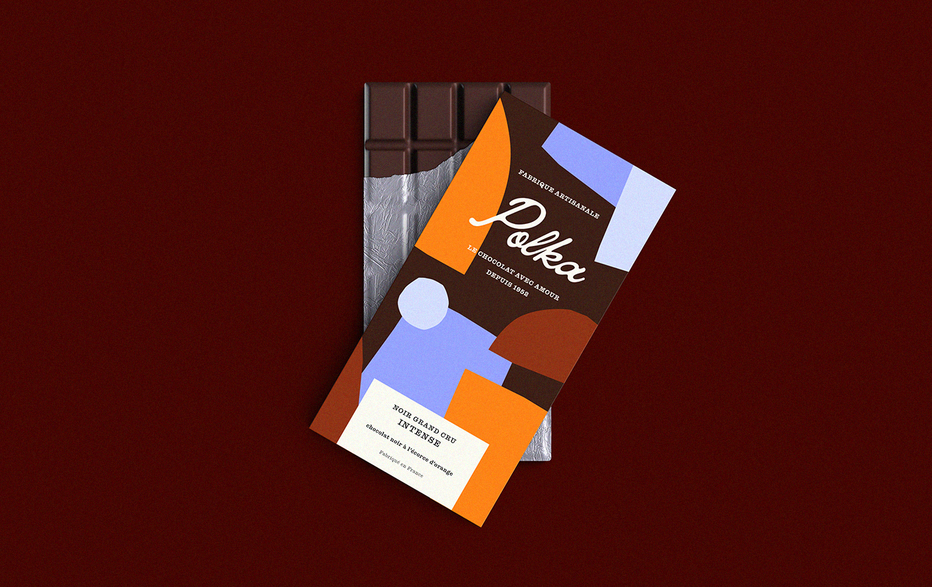 Tablette de chocolat noir emballée dans un emballage coloré avec un design abstrait, posé sur une surface rouge foncé.