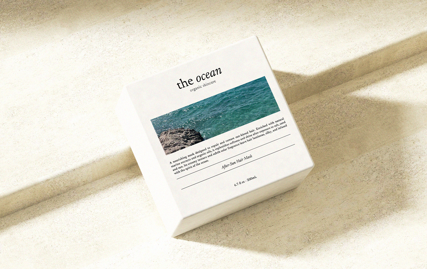 Une boîte de produits de soin appelée "the ocean" avec une image de la mer sur l'emballage, poser sur une surface éclairée par la lumière du soleil.