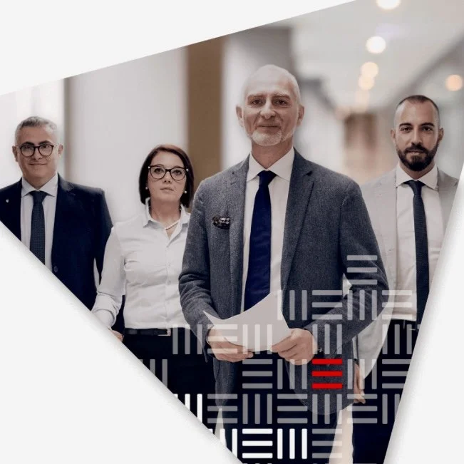 Quattro professionisti sorridenti in abiti formali in un ambiente moderno, evidenziando un giovane uomo con capelli corti e barba sulla destra e un adulto con capelli bianchi e barba al centro.