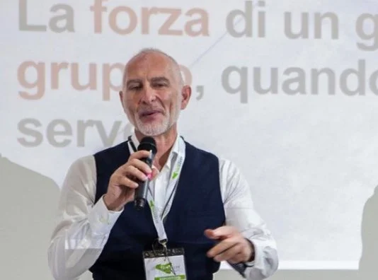 uomo che parla in pubblico con microfono, sfondo con testo in italiano