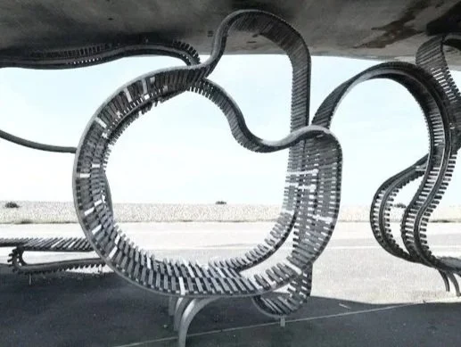 Modern metal sculpture resembling abstract looping shapes placed on a sidewalk.