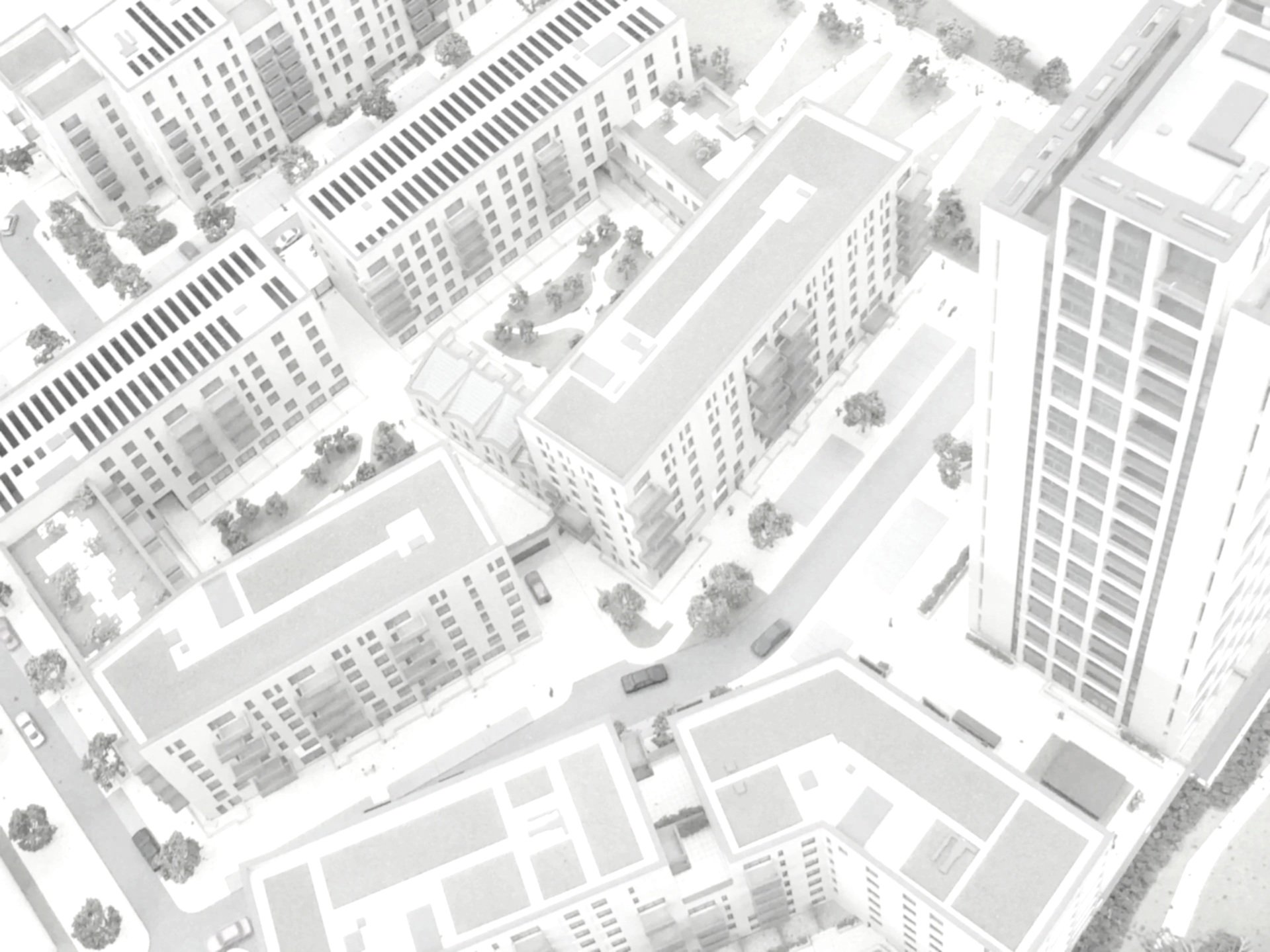 Aerial view of a city with high-rise and mid-rise buildings, streets, parked cars, and trees.