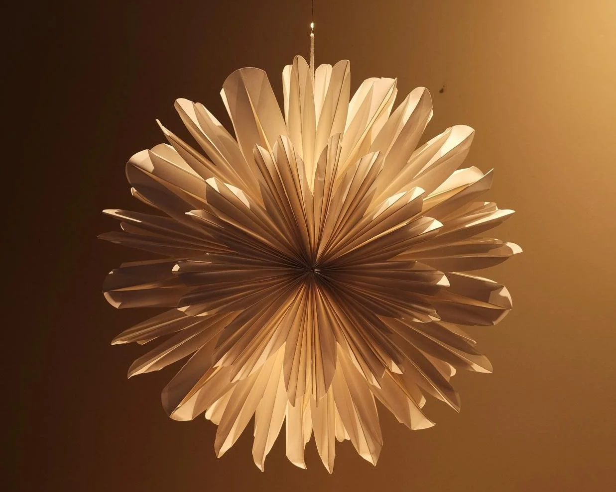 Decorative hanging paper ornament with a spherical shape, made of folded paper petals, lit from above.