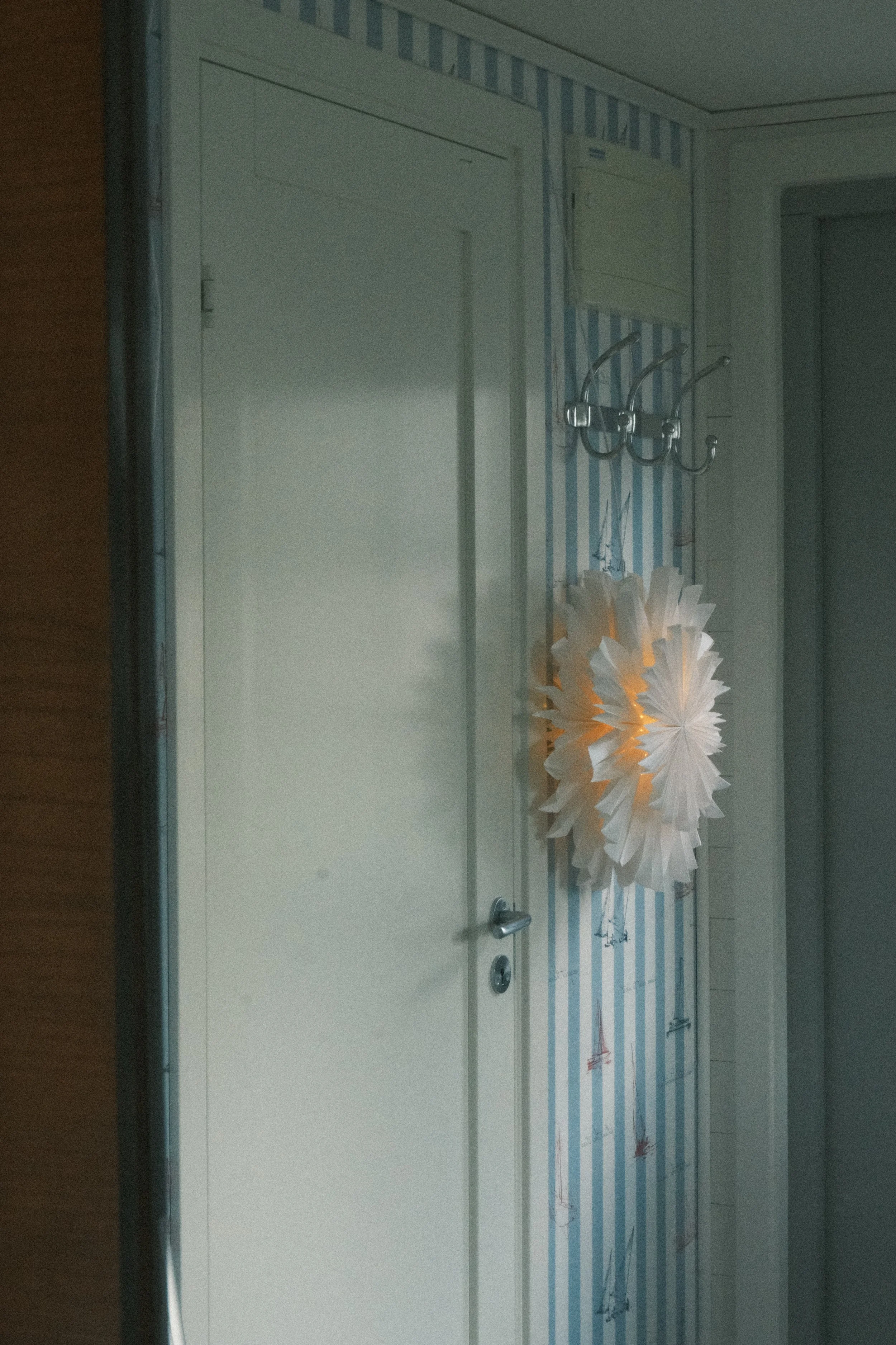 A white door with a handle on a room with striped wallpaper and a decorative paper lantern hanging on the wall.
