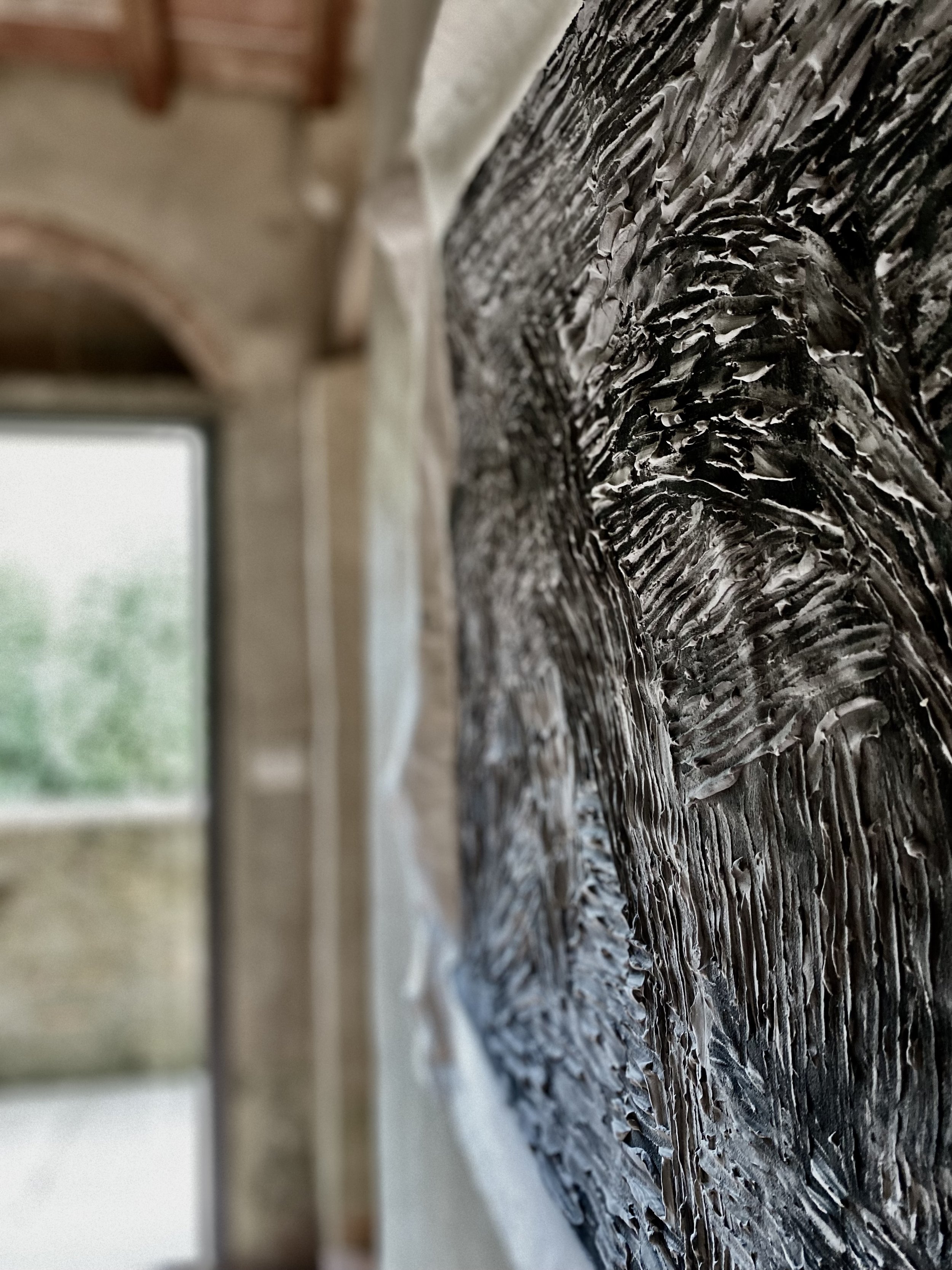 Nahaufnahme einer abstrakten, schwarzen und weißen Öl- oder Acrylmalerei auf Leinwand, im Innenraum einer rustikalen Atelier oder Werkstatt, mit Holzdecke und großem Fenster im Hintergrund.