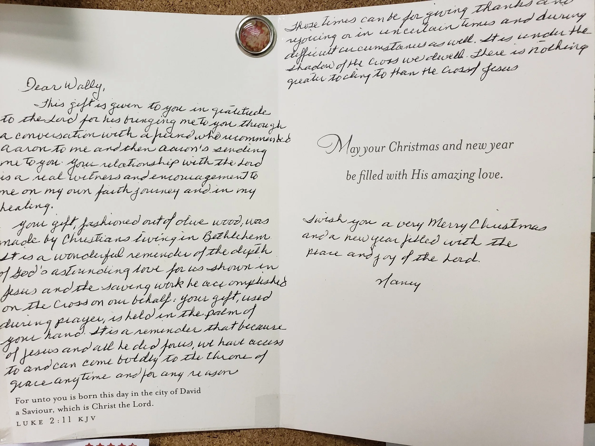 Open Christmas card with handwritten message and a small, round, decorative item attached at the top left corner.
