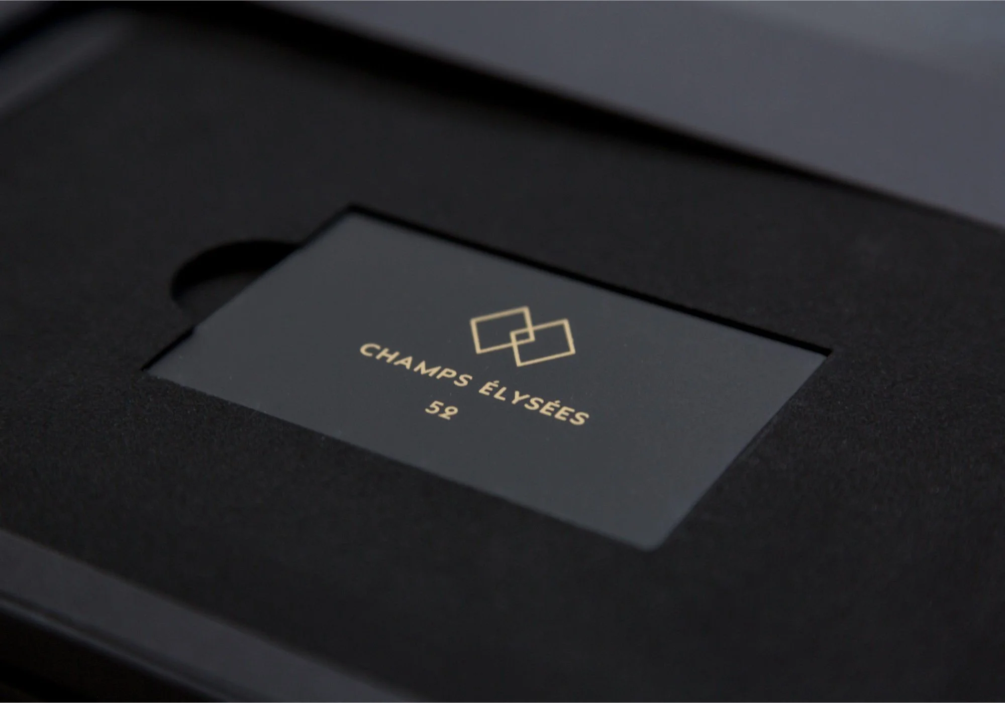 Une boîte noire contenant un coffret avec un logo doré de deux rectangles entrecroisés et le texte 'Champs Élysées 52'