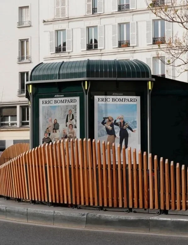 Un abri bus à Paris avec deux affiches publicitaires pour Eric Bompard, entouré d'une clôture en bois.