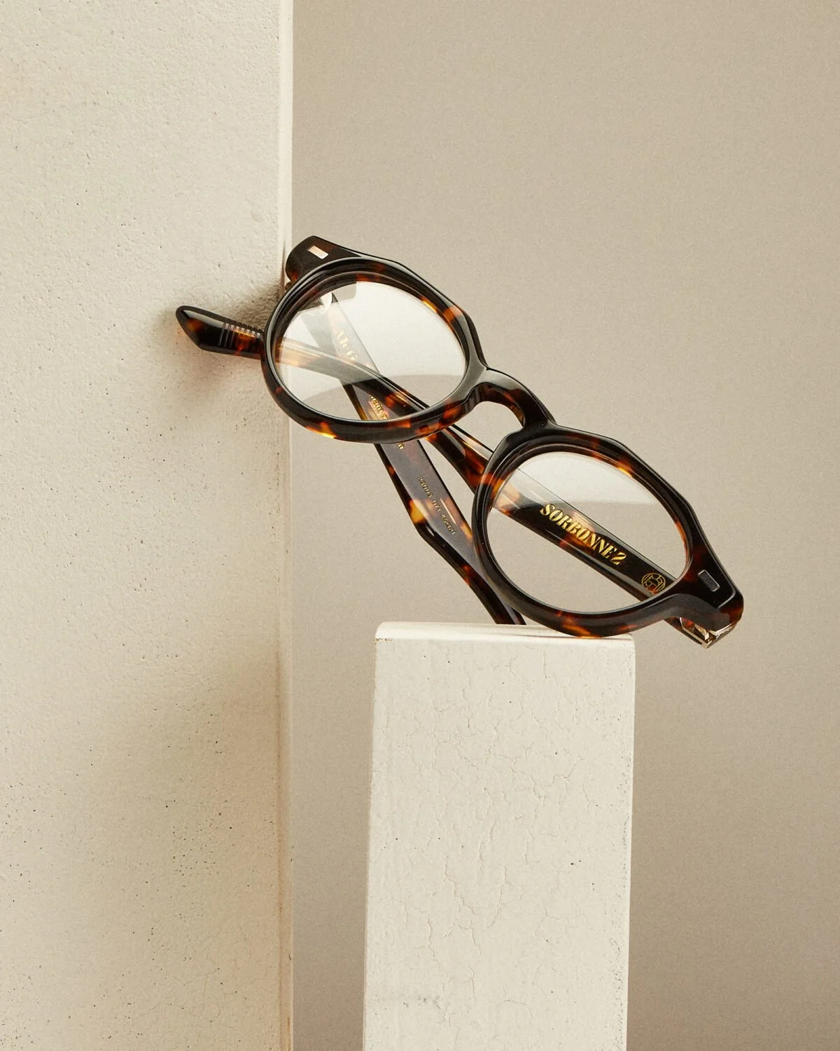 Lunettes à monture tachetée posées sur un socle blanc, contre un fond beige.