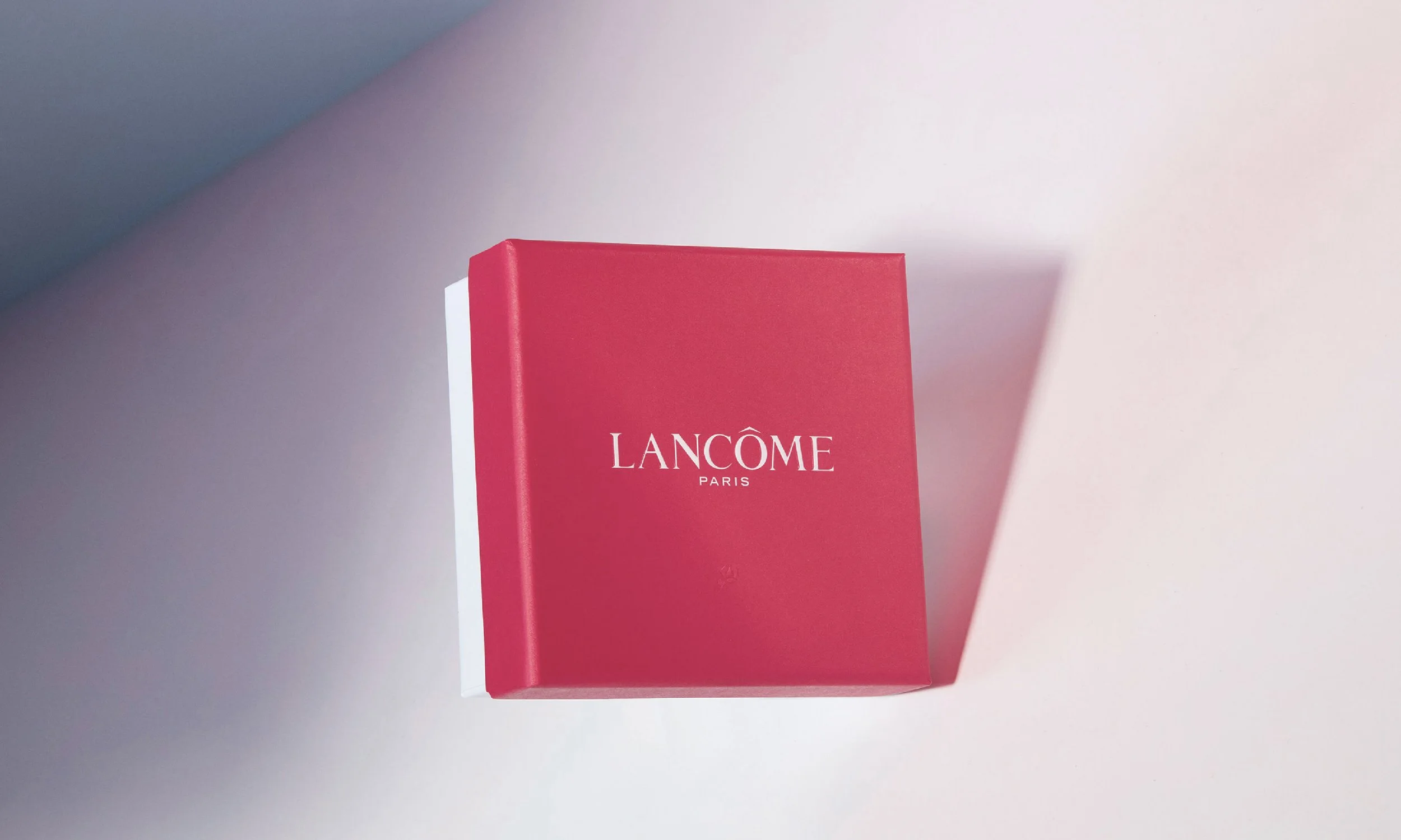 Boîte rouge de produits Lancôme Paris sur une surface blanche avec ombre.