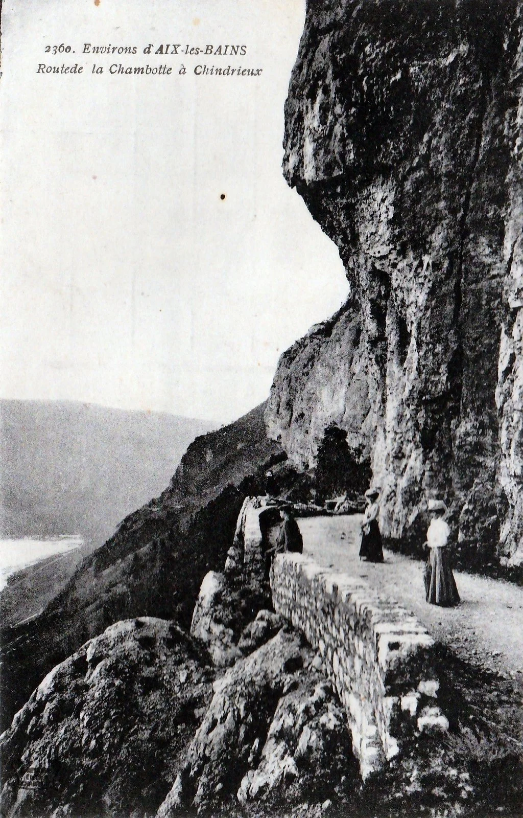 Photographie en noir et blanc d'un sentier côtier avec des rochers et des personnes marchant le long d'une falaise, avec la mer en arrière-plan, près d'Aix-les-Bains, route la Chambotte à Chindrieux.