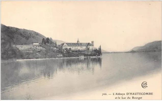 Une vieille photo en noir et blanc montrant un abbaye au bord d'un lac, avec des collines environnantes, intitulée "L'Abbaye D'HAUTECOMBE et le Lac du Bourget".