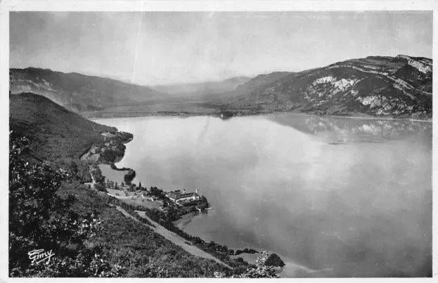 Paysage de lac entouré de montagnes avec quelques bâtiments en bas à gauche.