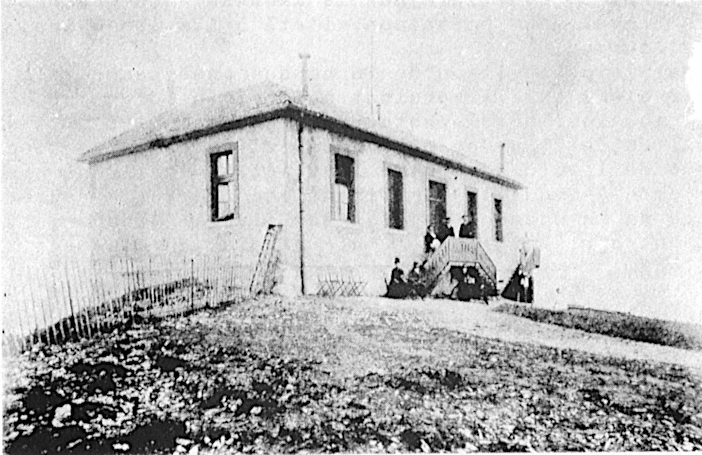 Photo en noir et blanc d'une maison avec des personnes sur l'escalier extérieur.