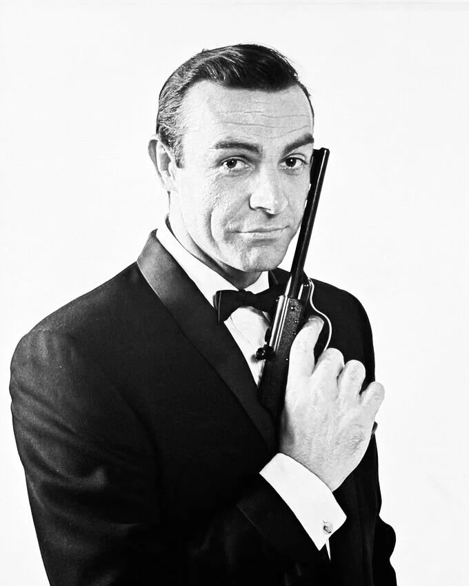 Sean Connery as James Bond in a tuxedo holding a gun