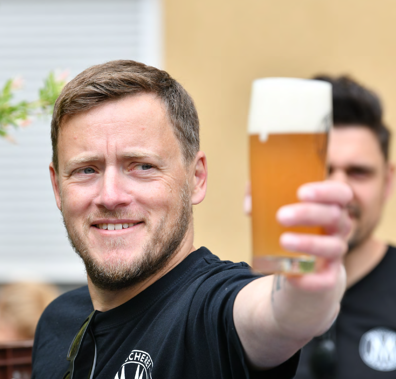 One smiling man raising a glass of beer outdoors