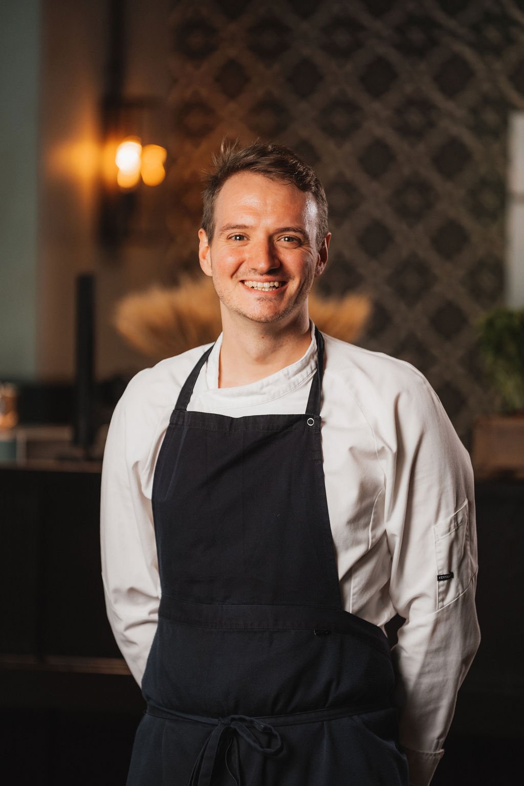 Chef de Cuisine Filippo Zuccagnoli  in a white chef's coat and black apron standing in front of the live kitchen of Schwabinger Tor Bräu WIrtshaus.