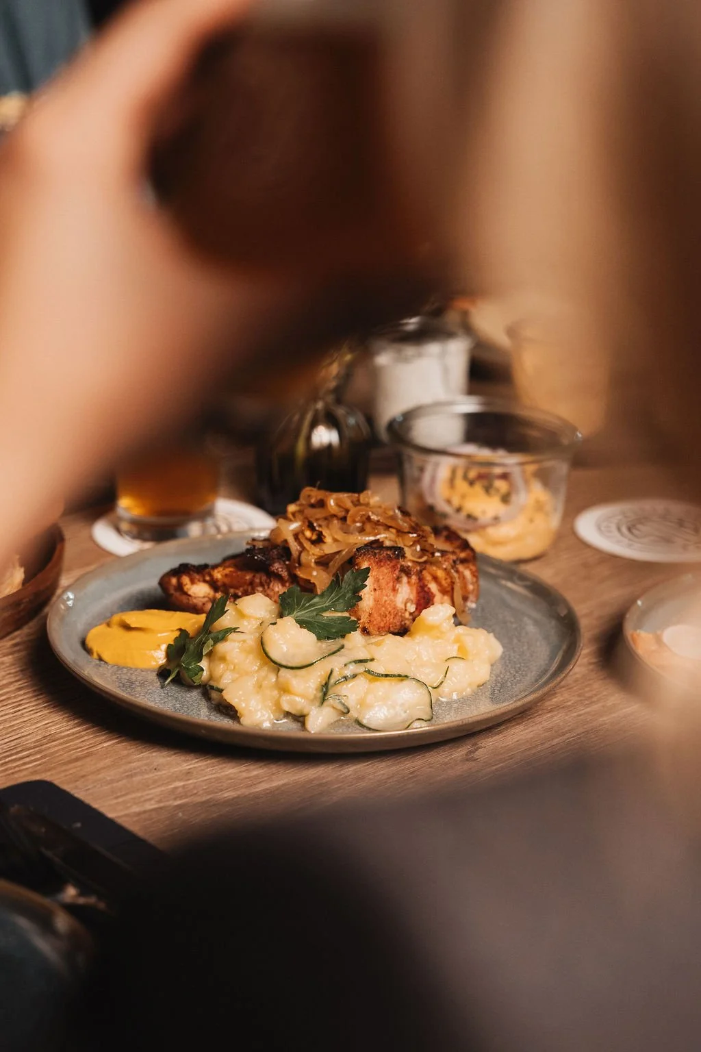 Plate of grilled chicken topped with sautéed onions, served with mashed potatoes and garnished with parsley, on a rustic wooden table.