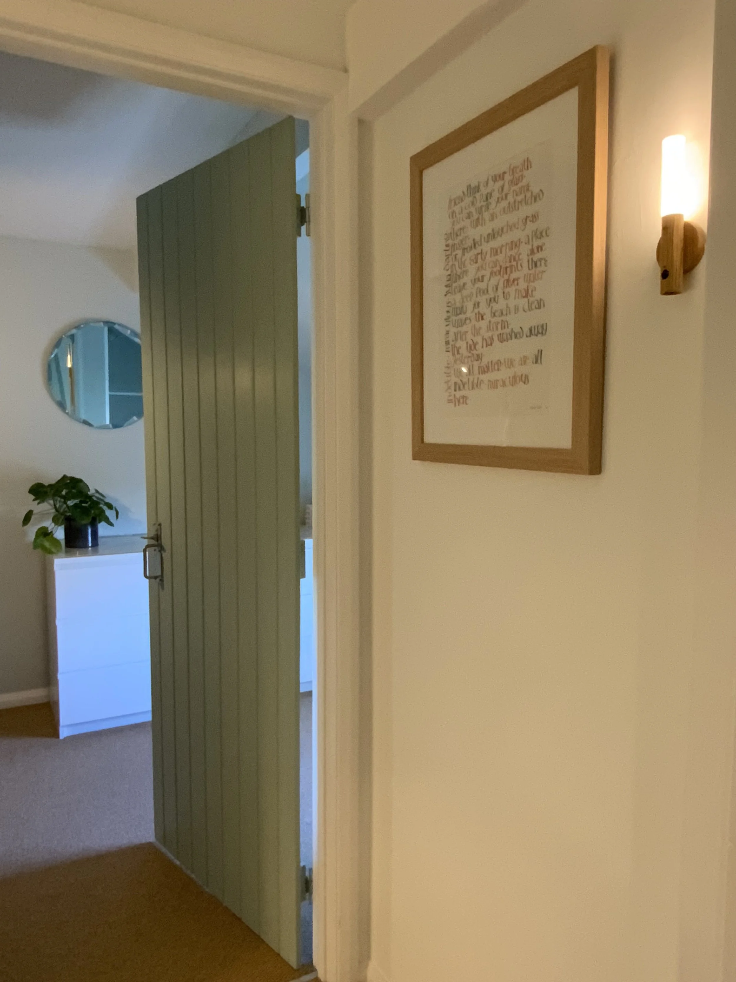 Hallway with open door, framed wall art, round mirror, and a potted plant on a dresser.