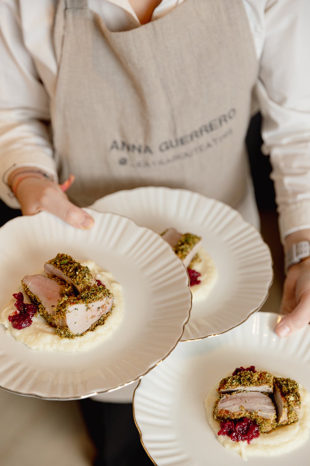 Person wearing an apron holding plates with breaded and sliced meat, served on a bed of mashed potatoes with red sauce.