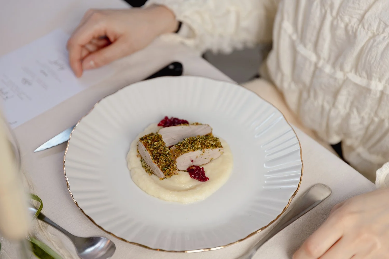 A plated dish with sliced poultry coated in herbs, served on a bed of creamy mashed potatoes with a dollop of red sauce on the side.