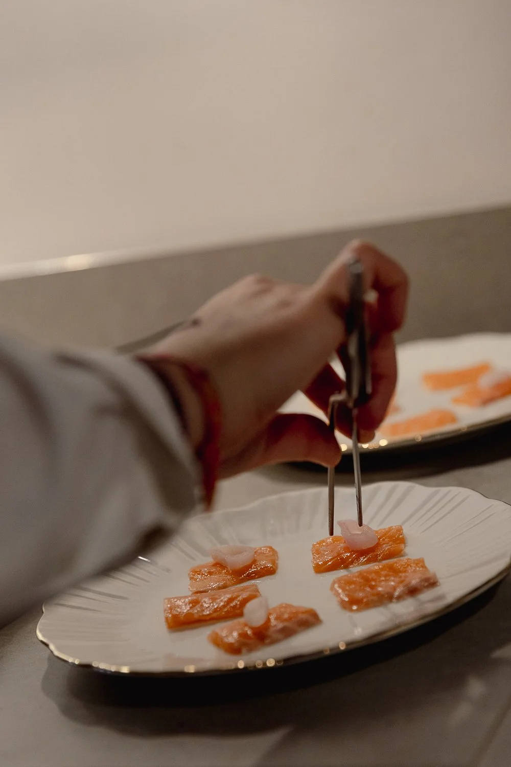 Person placing small pieces of sashimi on a white plate with chopsticks