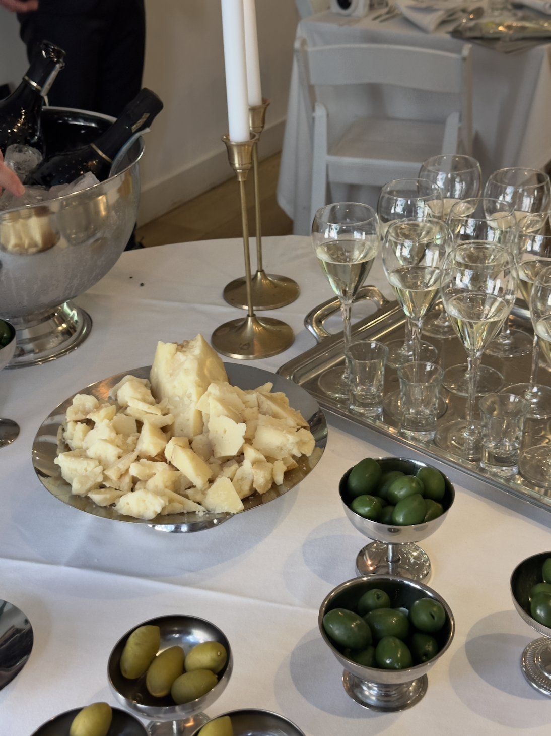 Cheese, green olives, yellow olives, and glasses of champagne on a white tablecloth at an event or celebration.