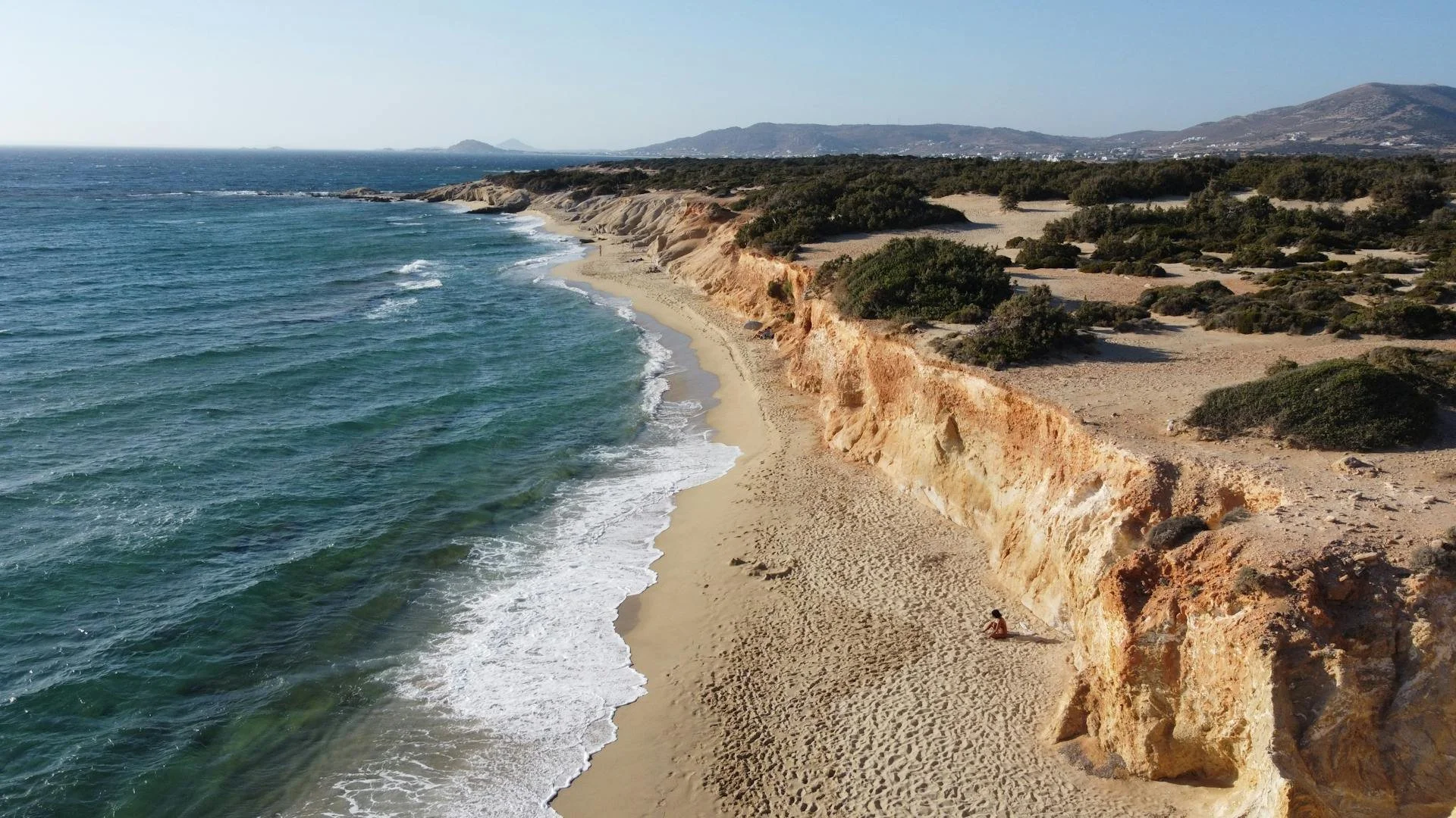 Secluded beach with golden cliffs, sandy shore, and blue ocean waves under a clear sky