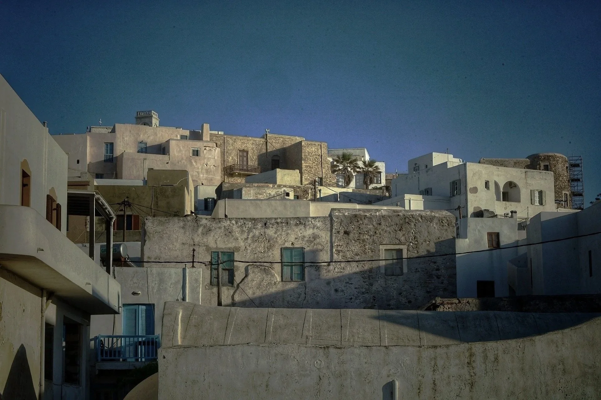 Whitewashed buildings on a hillside in Naxos, Greece, under a cloudy sky.